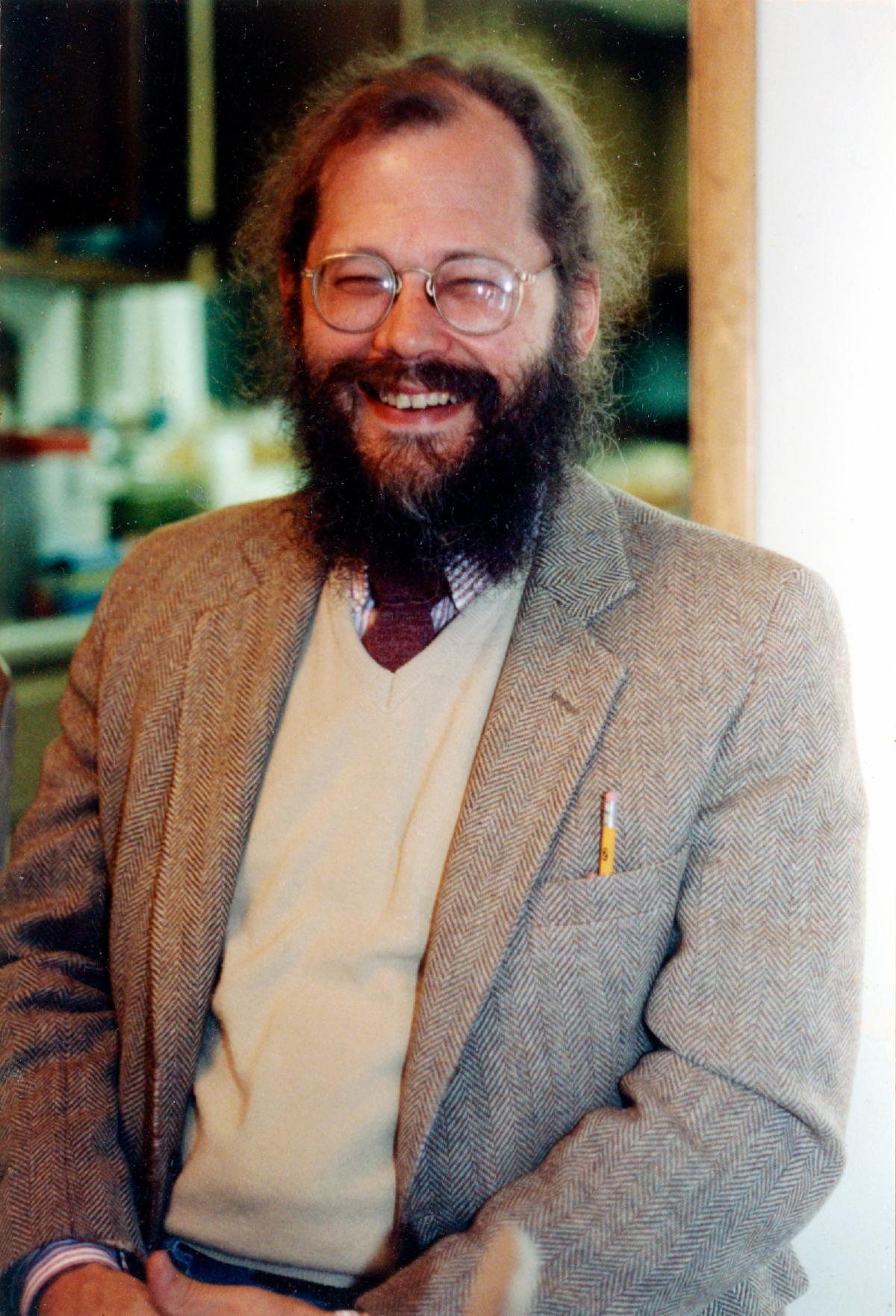 Bearded man in glasses, jacket, vest, and tie smiling