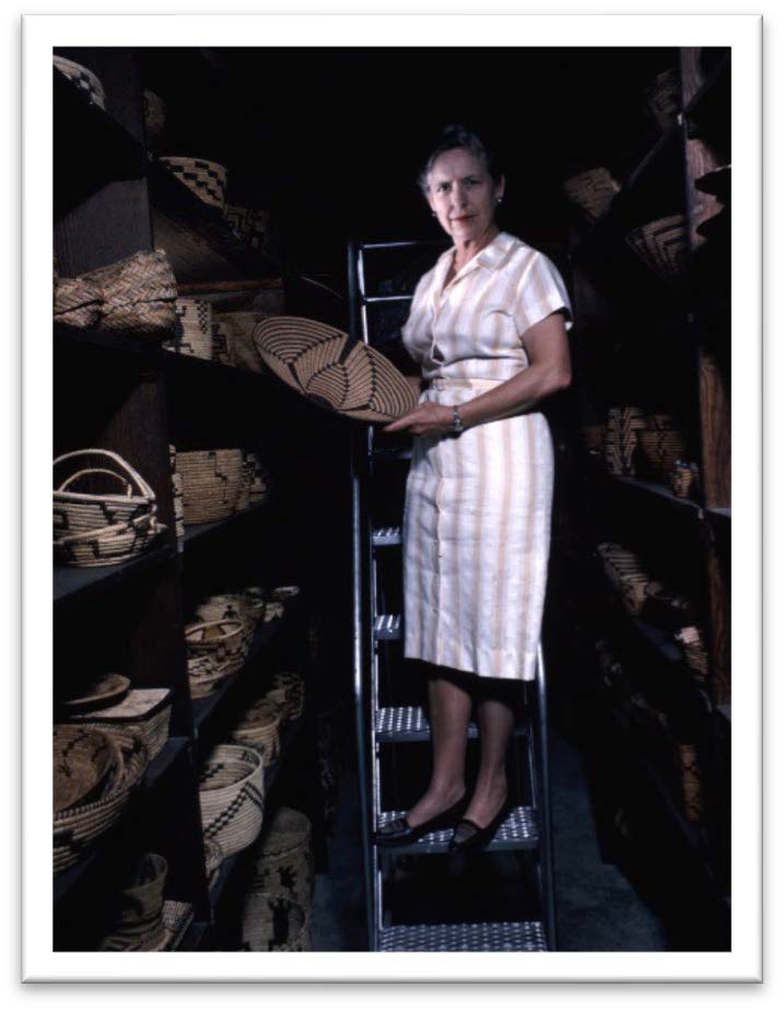 woman standing on ladder in storage room full of baskets, holding a basket
