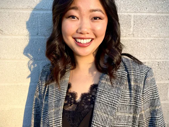 a woman with medium length black hair smiling with a concrete wall behind her