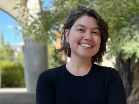 A woman with short brown hair wearing a black shirt smiling with trees behind her