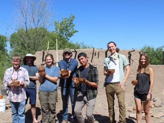 Seven field school participants holding pots they made