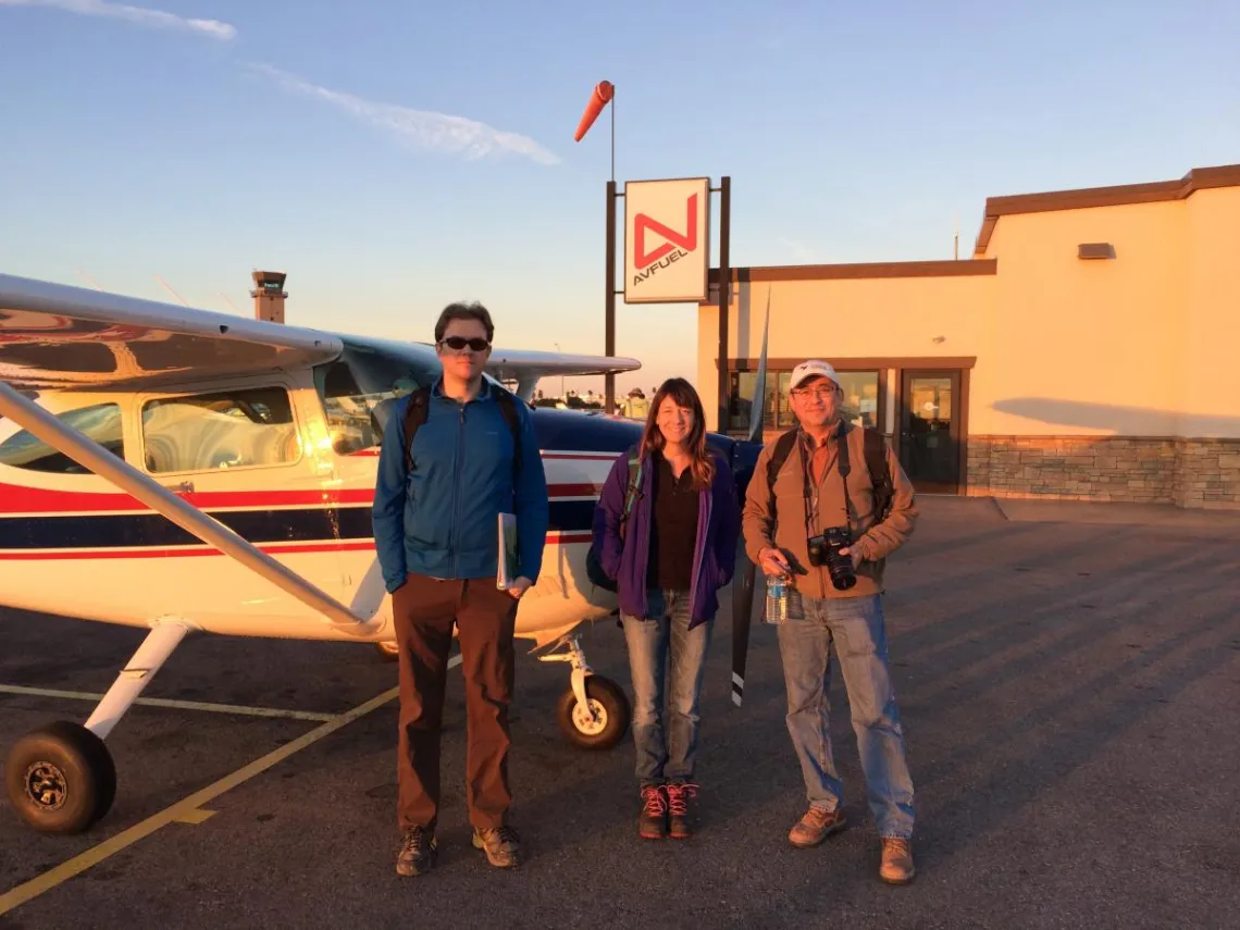 three people in front of plane during sunset