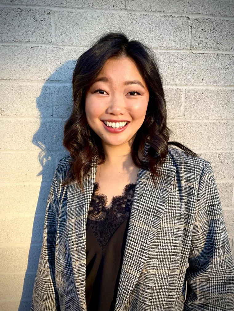 a woman with medium length black hair smiling with a concrete wall behind her