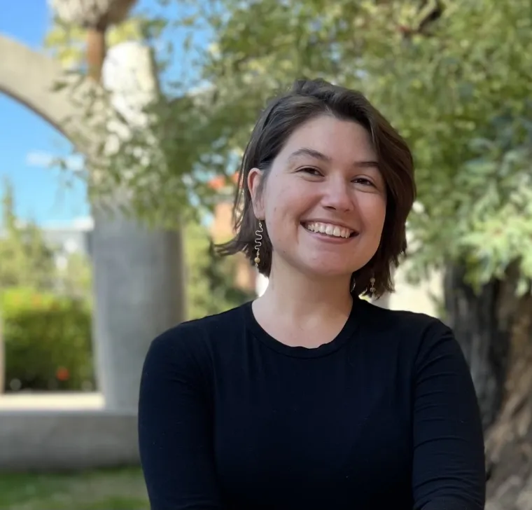 A woman with short brown hair wearing a black shirt smiling with trees behind her