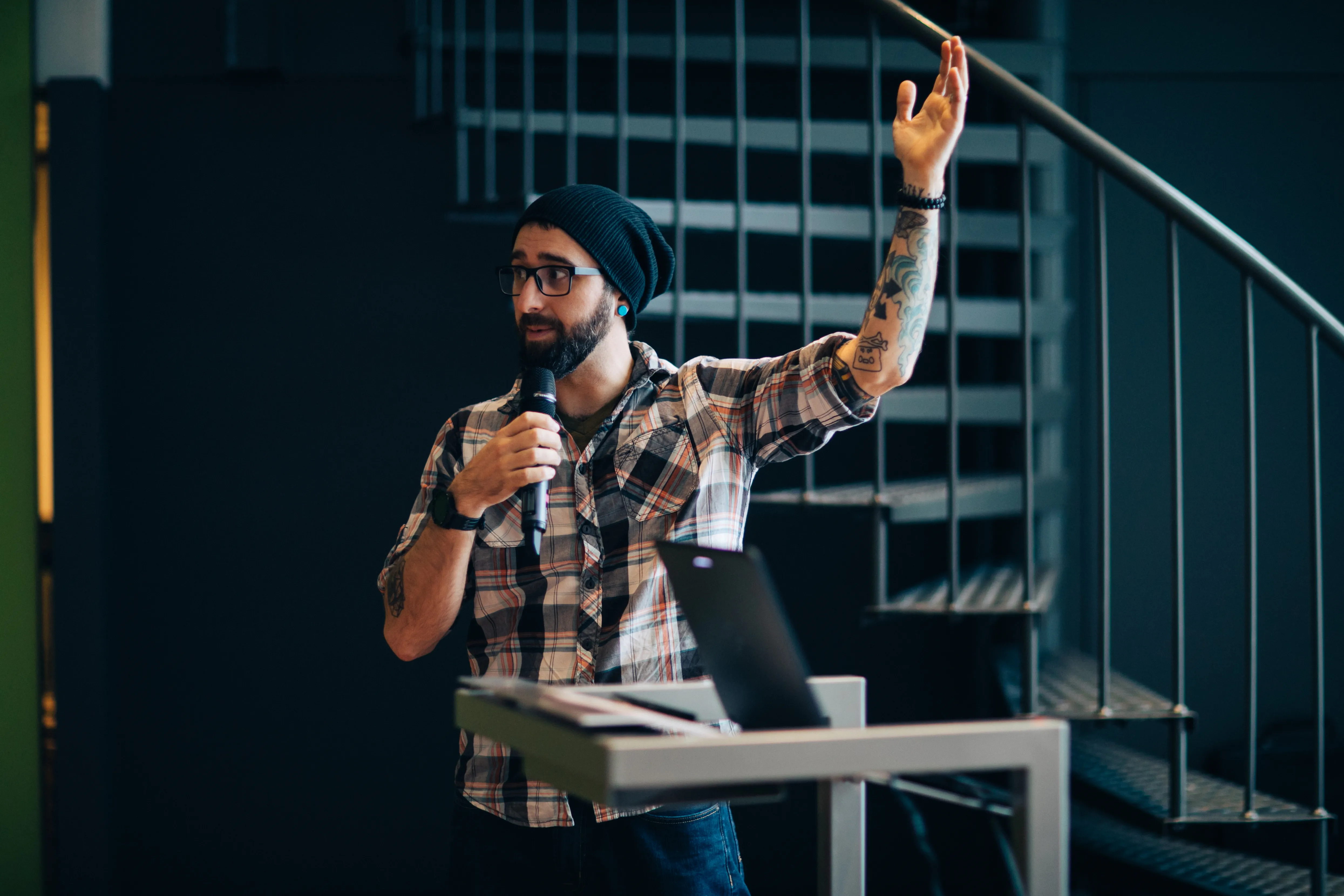 Bearded man in black knit cap holding microphone, one arm upraised