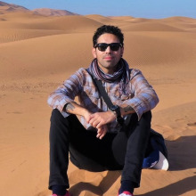 Ismael Sanchez, wearing sunglasses, seated in sand dunes
