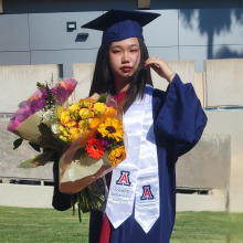 Katherine Tu in academic regalia with bouquets of colorful flowers
