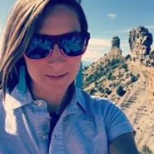 woman in sunglasses and blue shirt in front of desert scenery