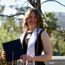 Sarah Yockey in front of a tree, with academic stole and holding graduation cap