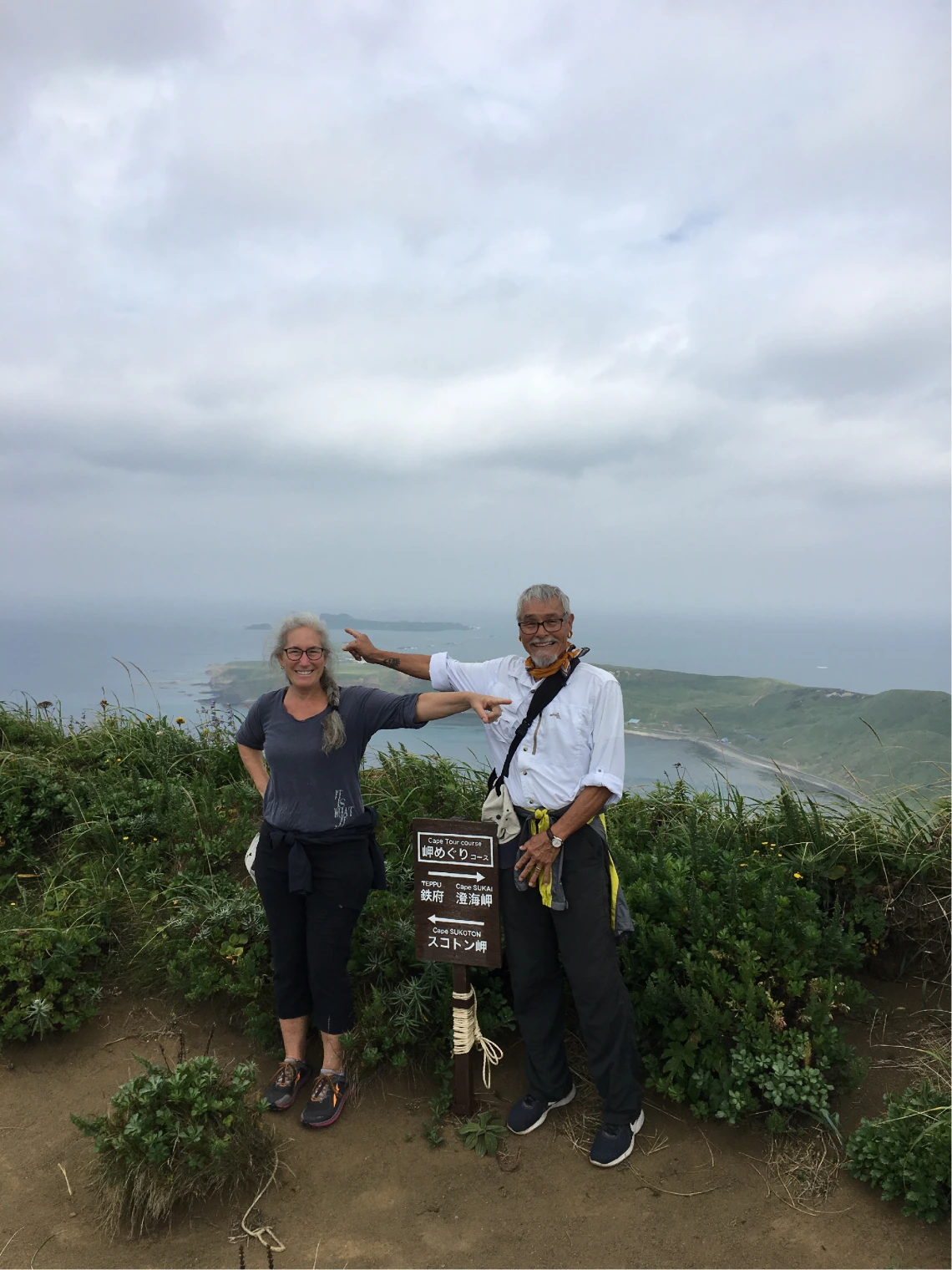 Dr. Joe Watkins and Carol Ellick on a hike near a high point on the hike on Rebun Island A woman and a man pointing in opposite directions