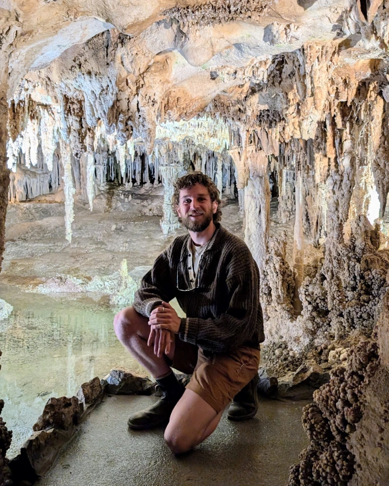 Hammarstrom kneeling on one knee with stalactites and stalagmites in the background